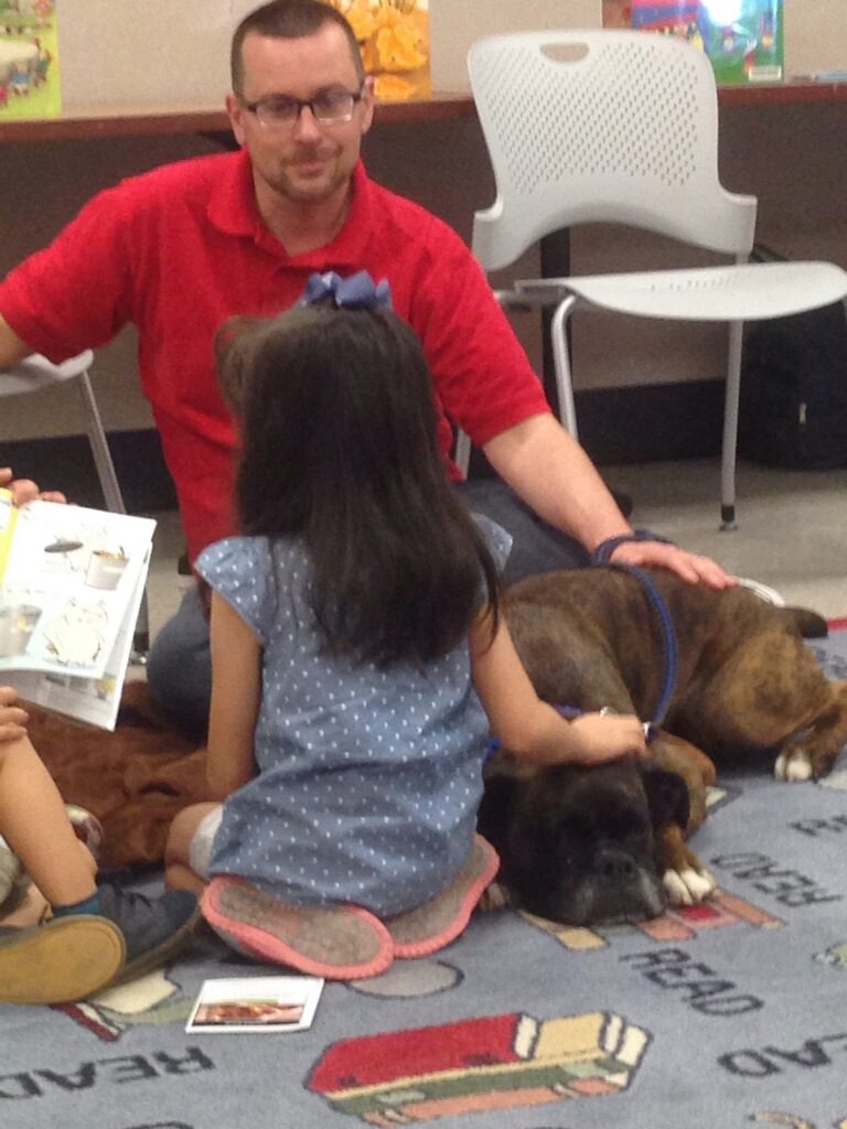 Tim sitting with Zeus and a young girl reading a book during a school therapy visit